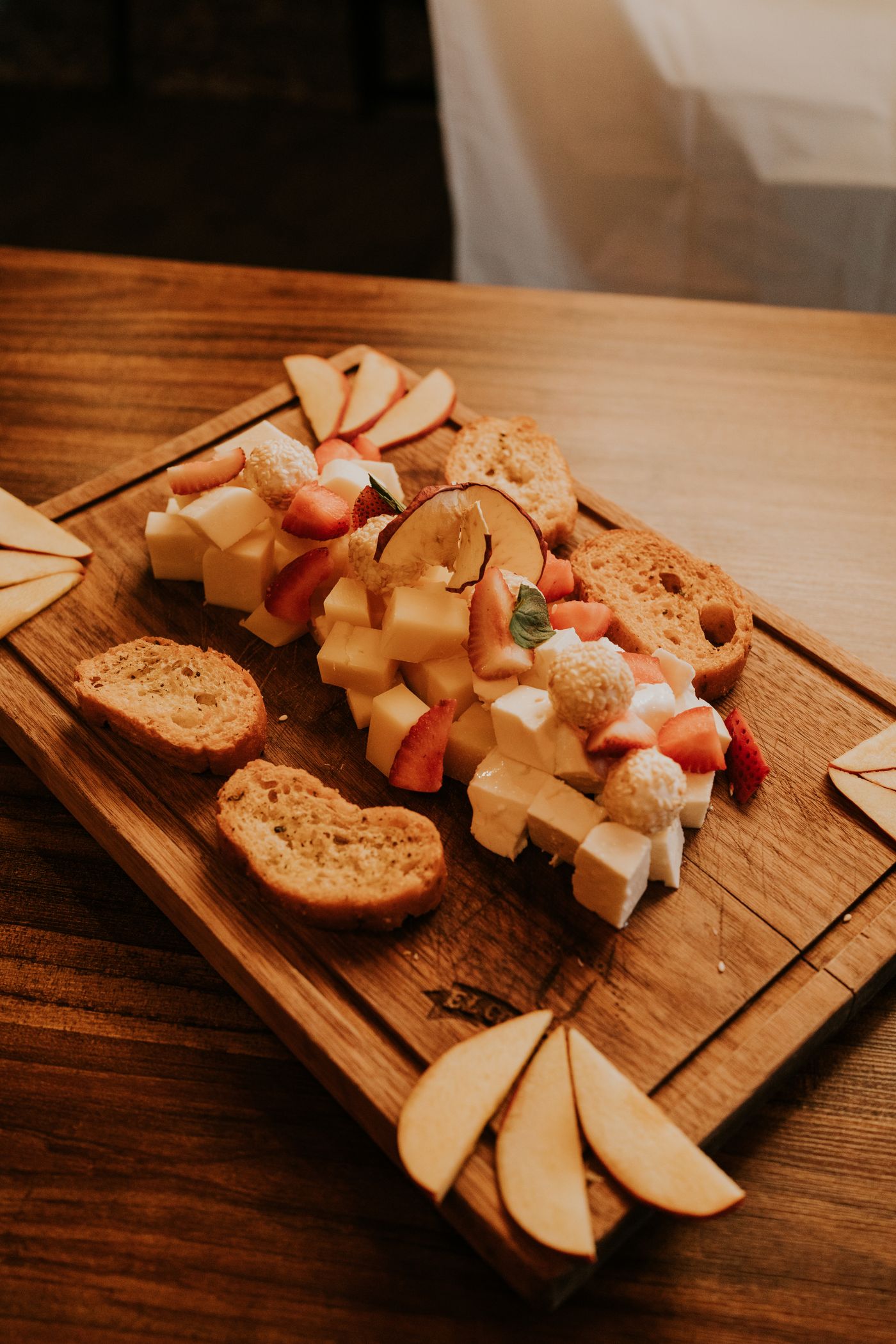 Houten plank met kaasblokjes, vers fruit en brood